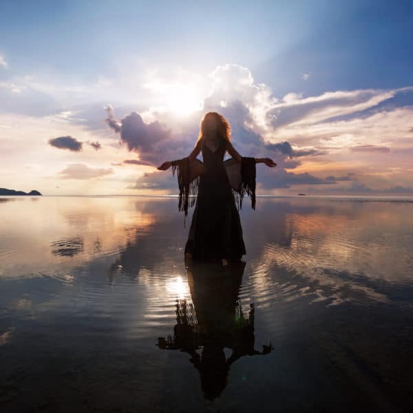Elegant woman walking on water. Sunset and silhouette.